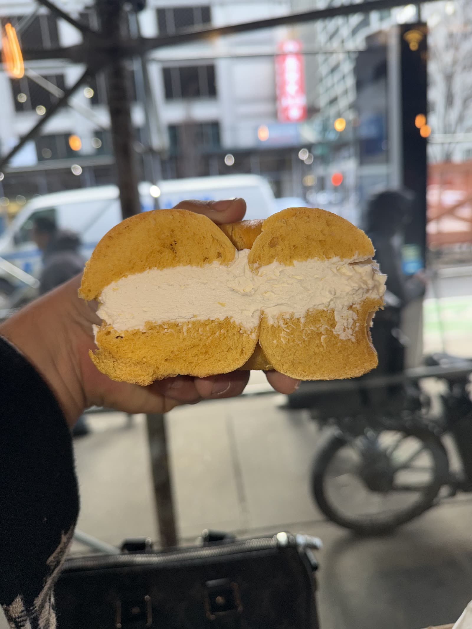 A cannoli style cream filled sandwich held up on a city sidewalk